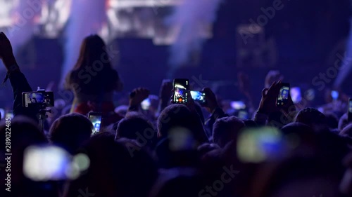 Fires lighting, flashes blinking and smokes coming out during show on rock concert. Spectators watching show and shooting videos with their smartphones. Blue light. 4K photo