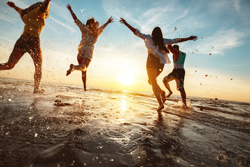 Happy friends at beach party runs to sunset water