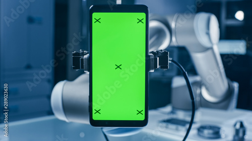 Real Robot Arm Holding Green Mock-Up Screen Smartphone Device. Industrial Robotic Manipulator End Effector Holds Mobile Phone with Chroma Key Display. Modern Manufacturing Facility / Laboratory 
