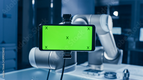 Robot Arm Holding Green Mock-up Screen Smartphone in Landscape Mode. Industrial Robotic Manipulator End Effector Holds Mobile Phone with Chroma Key Display. 