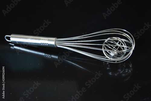 A beautiful metal whisk for whipping, stirring yolks and proteins, kitchen utensils for the kitchen are located on a black glossy surface.