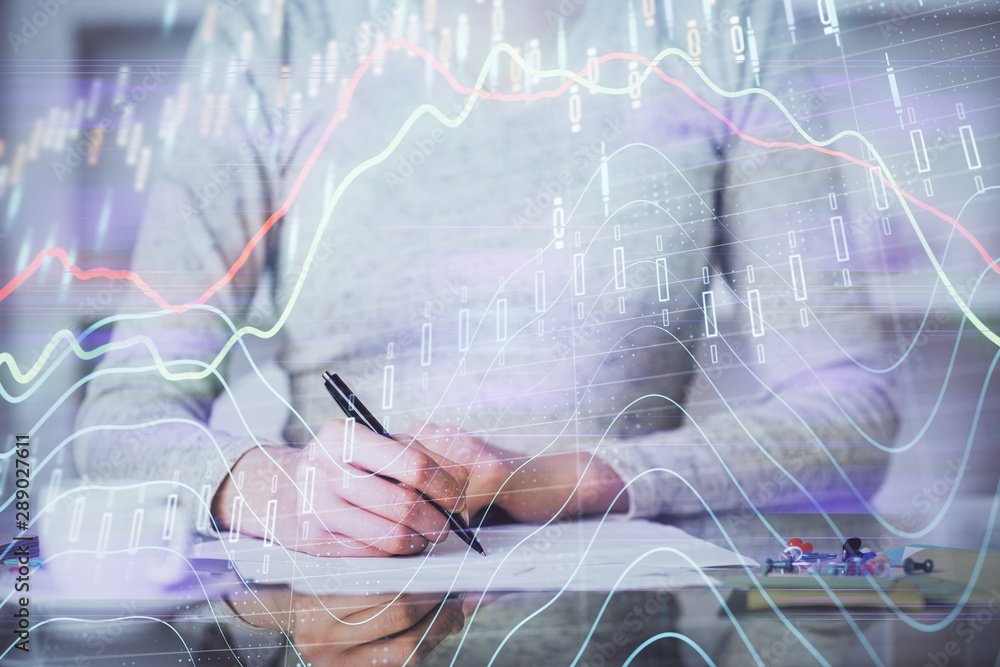 Hand taking notes in notepad. Forex chart holograms in front. Concept of research. Multi exposure Hand taking notes in notepad. Forex chart holograms in front. Concept of research. Multi exposure