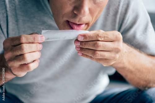cropped view of man in t-shirt licking paper for blunt