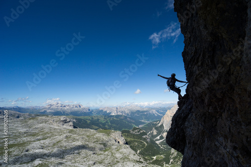 attractive blonde female climber in silhouette on a steep Via Ferrata pointing to the sky