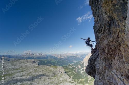 attractive blonde female climber on a steep Via Ferrata pointing to the sky