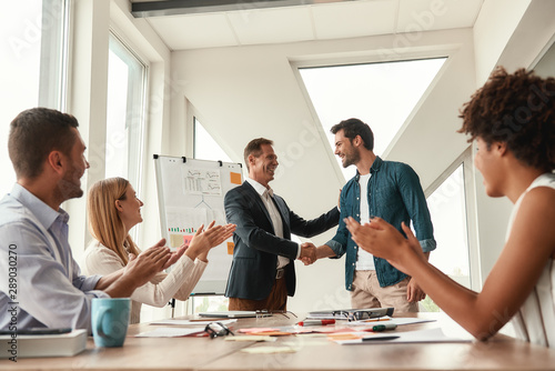 Welcome to our team Two cheerful colleagues shaking hands and smiling while having a meeting in the modern office photo