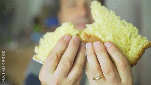 Satisfied handsome mature man breaking a soft slice, eating and chewing an Italian Pandoro, a typical Christmas cake, as a good eater and he's enjoying the food.