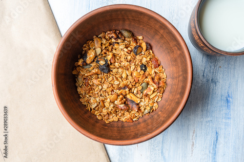 Granola in a brown clay bowl with a glass of milk. Tasty and healthy breakfast. Blue wood background. Top view. Flat lay food