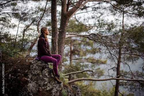 Girl sitting on the rock in the forest looking at the distance