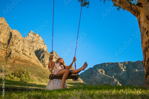 Beautiful woman swinging on a swing in nature with Table Mountain in the background.