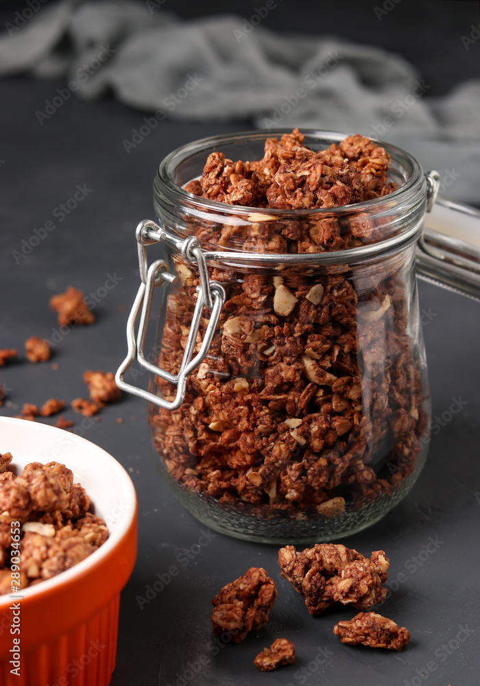 Granola crispy muesli with natural honey, chocolate and nuts in a glass jar against a dark background, healthy food, vertical orientation Granola crispy muesli with natural honey, chocolate and nuts in a glass jar against a dark background, healthy food, vertical orientation