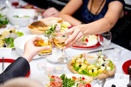 man and woman clink glasses with glasses over a served table at a holiday. Close-up without faces