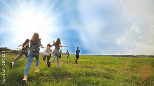 Happy friends run against the backdrop of a beautiful sky and sun.