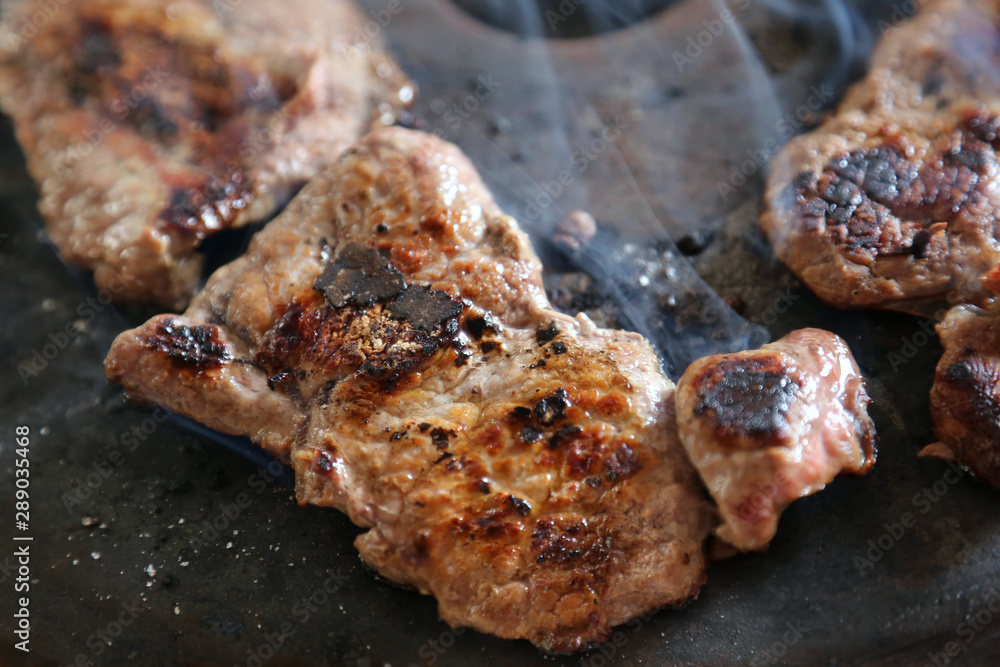 Simple cooking.The meat is fried on a black primitive black roasting pan and slightly charred. Hot steam flows over the dish. Simple cooking.The meat is fried on a black primitive black roasting pan and slightly charred. Hot steam flows over the dish.