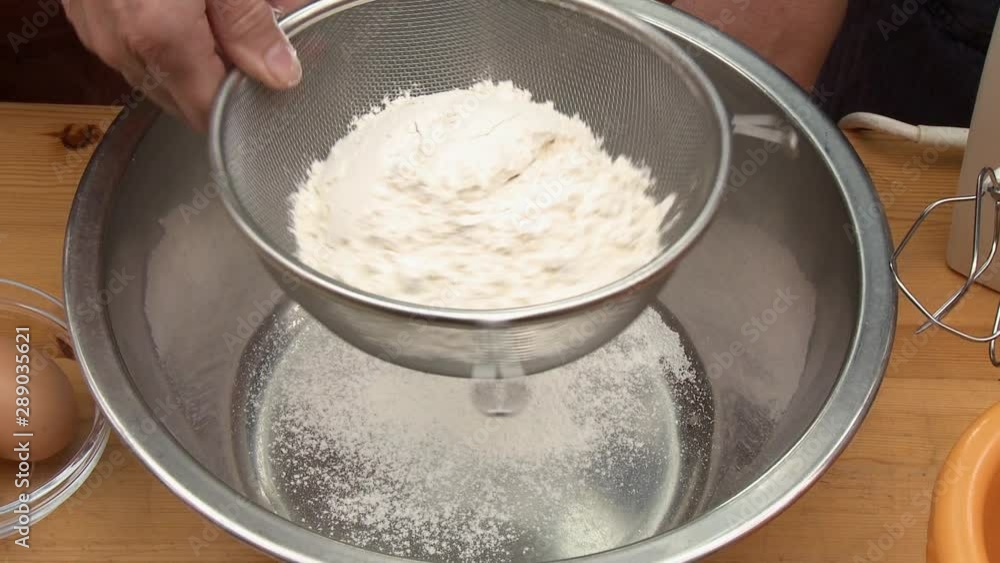 Handheld, medium close up shot of a person straining flour and whole wheat flour into a metal bowl. Handheld, medium close up shot of a person straining flour and whole wheat flour into a metal bowl.