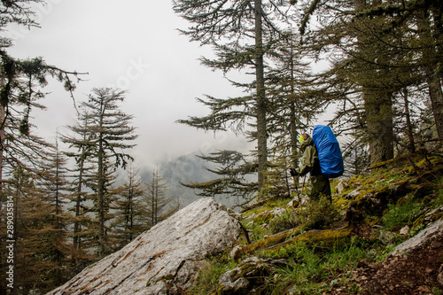 Girl in the raincoat standing on the rock with hiking backpack and sticks