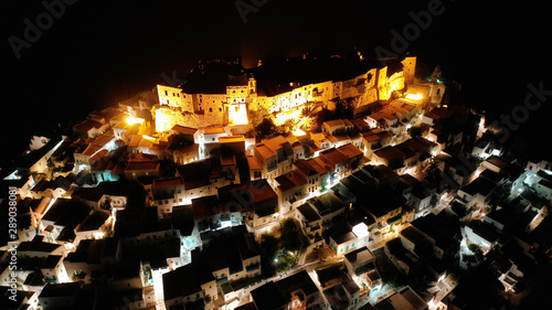 Aerial drone night shot of iconic illuminated medieval fortified castle overlooking the deep blue Aegean sea in Chora of Astypalaia  Dodecanese islands  Greece