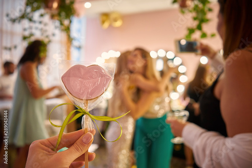 woman holds candy in her hands in the form of lips  in the background women are hugging. a party