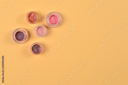 Cosmetics. Makeup. Jars with crumbly bright shadows, glitter. Pink,peach, golden colors on beige background. Closeup. Space for text or design.