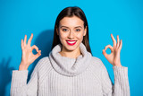 Portrait of charming millennial showing promo smiling at camera wearing gray jumper isolated over blue background