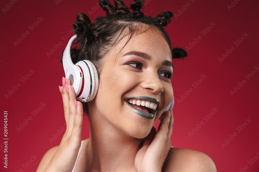 Fototapeta premium Image of extreme punk girl with bizarre hairstyle and dark lipstick smiling while listening to music with headphones