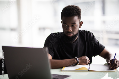 Young African man looking at camera with laptop in modern office