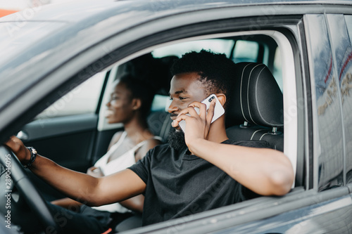 Young african man talking phone while drive car near his woman