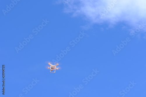 White drone quadcopter flying on the air for take a photo and video with white cloudy and blue sky background.