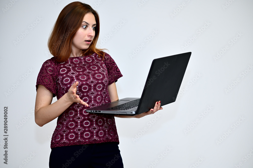 Portrait of a brunette girl with beautiful brown hair in a purple t-shirt with a laptop in hand on a white background. He stands in different poses, demonstrates emotions. Portrait of a brunette girl with beautiful brown hair in a purple t-shirt with a laptop in hand on a white background. He stands in different poses, demonstrates emotions.