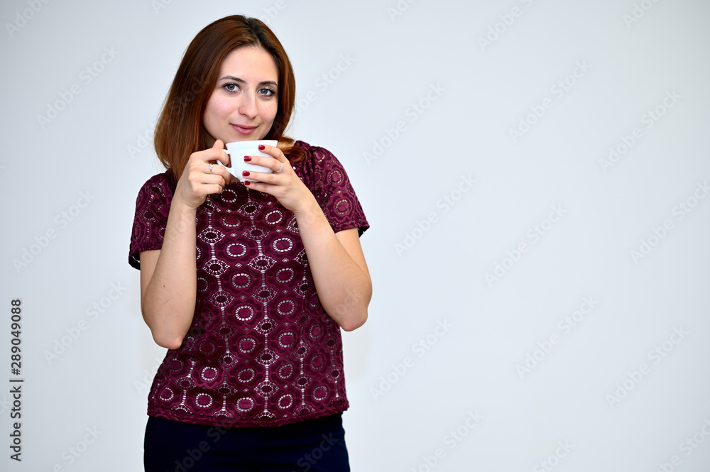 Portrait of a brunette girl with beautiful brown hair in a purple t-shirt with a cup of coffee in hand on a white background. He stands in different poses, demonstrates emotions. Portrait of a brunette girl with beautiful brown hair in a purple t-shirt with a cup of coffee in hand on a white background. He stands in different poses, demonstrates emotions.
