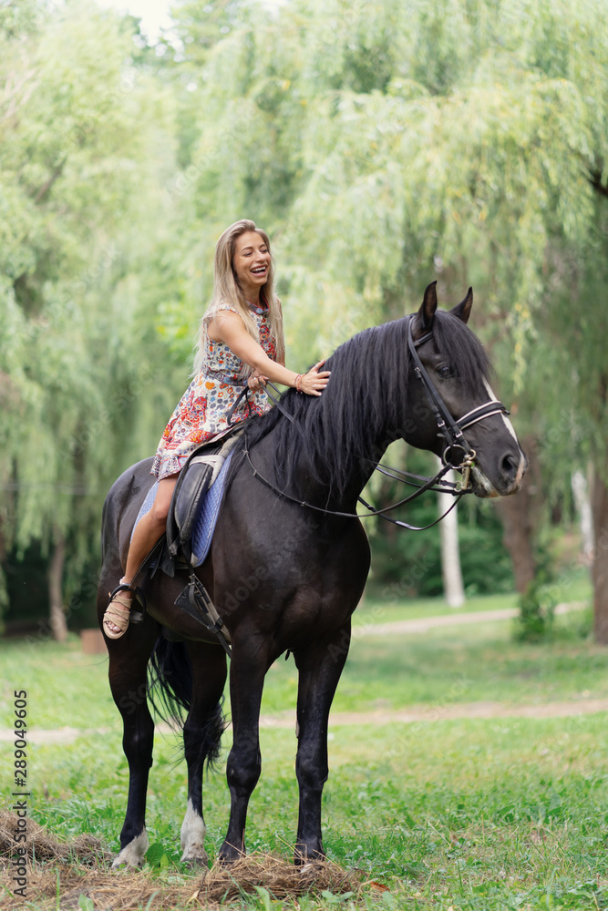 Young woman in a bright colorful dress riding a black horse Young woman in a bright colorful dress riding a black horse