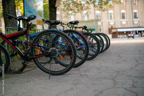 row of many bicycles parked on the public city rent in the park on a summer season, weekend activitiy.