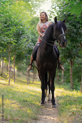 Young woman in a bright colorful dress riding a black horse