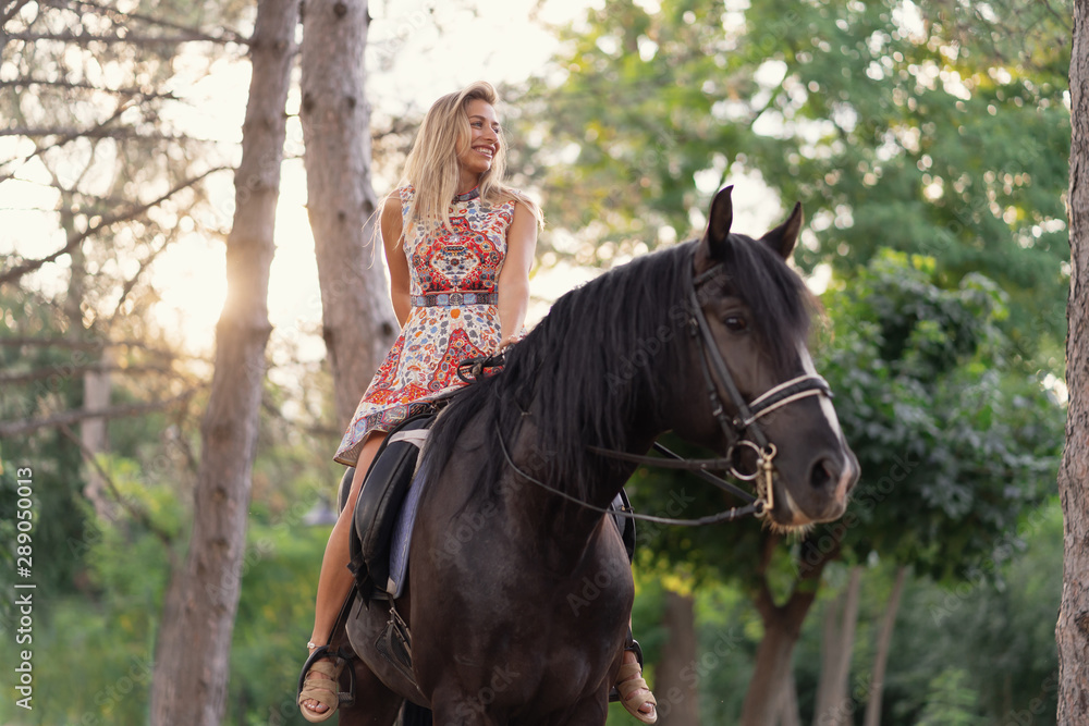 Young woman in a bright colorful dress riding a black horse Young woman in a bright colorful dress riding a black horse