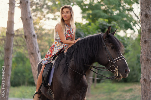 Young woman in a bright colorful dress riding a black horse