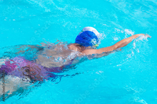 Senior caucasian woman in activity swimming in freestyle stroke. Pratice sport in the swimming pool. Outdoor under the sunlight. With swimming cap and goggles. Healthy lifestyle © luciano