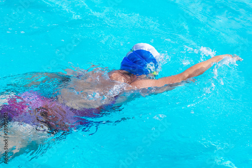 Senior caucasian woman in activity swimming in freestyle stroke. Pratice sport in the swimming pool. Outdoor under the sunlight. With swimming cap and goggles. Healthy lifestyle