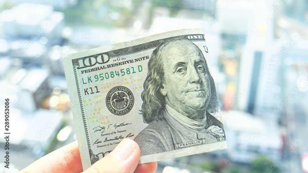Fingers holding 100 United States Dollars Banknote against Beautiful Cityscape Fingers holding 100 United States Dollars Banknote against Beautiful Cityscape