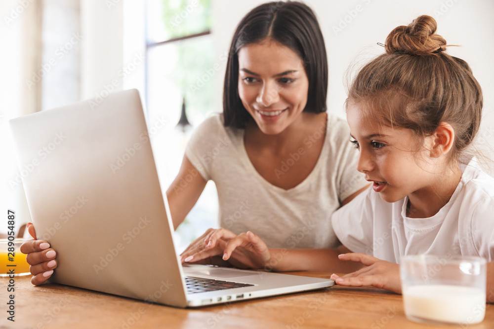 Image of happy family woman and her little daughter smiling and using laptop computer in apartment Image of happy family woman and her little daughter smiling and using laptop computer in apartment