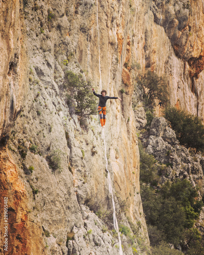 A man is walking along a stretched sling. Highline in the mountains. Man catches balance. Performance of a tightrope walker in nature. Highliner on the background of valley.