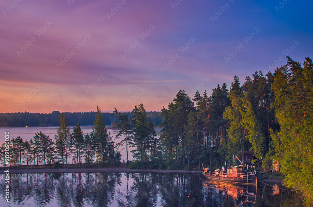 Small fishing or pleasure boat boat moored on Paijanne lake. Beautiful sunrise scape with stone beach, pine forest and water. Lake Paijanne, Finland.