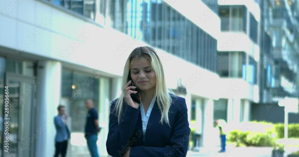 Young blonde office girl talking on the phone in front of office buildings.Eye level, close up, slow motion Young blonde office girl talking on the phone in front of office buildings.Eye level, close up, slow motion