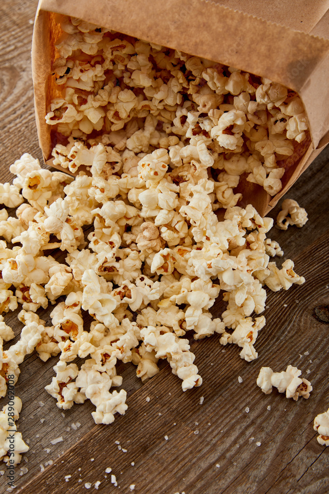 tasty popcorn scattered from paper bag on wooden background tasty popcorn scattered from paper bag on wooden background
