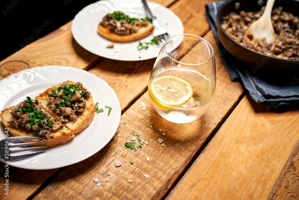 Toasts with mushrooms on white plate on wooden kitchen table