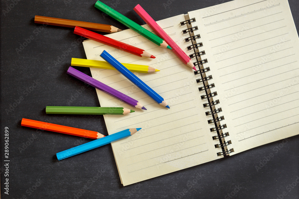 Back to school. Colored pencils and notebook on chalkboard Back to school. Colored pencils and notebook on chalkboard