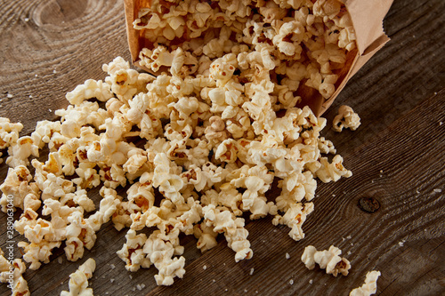 delicious crispy popcorn scattered from paper bag on wooden background