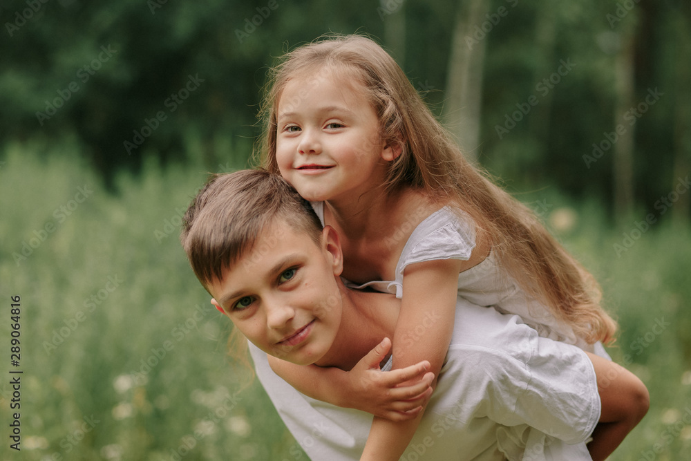 brother holds sister on shoulders outdoors in summer brother holds sister on shoulders outdoors in summer