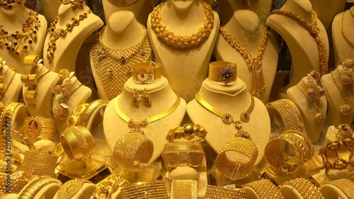 Precious gold necklaces, earrings and bracelets on rotating stands. Many gold jewelry with precious stones in a jewelry store window.