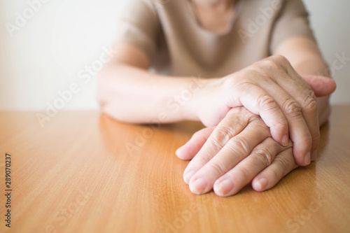 Parkinson's disease symptoms. Close up of tremor (shaking) hands of Middle-aged women patient on wooden table. Mental health and neurological disorders concept. Copy space.