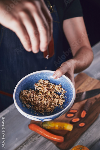 Young chef in kitchen holding bowl with walnut and preparing dinner. Food concept.